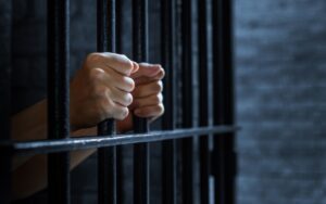 A person holding onto the bars of a jail cell from inside. Learn about whether you can bail yourself out of jail.